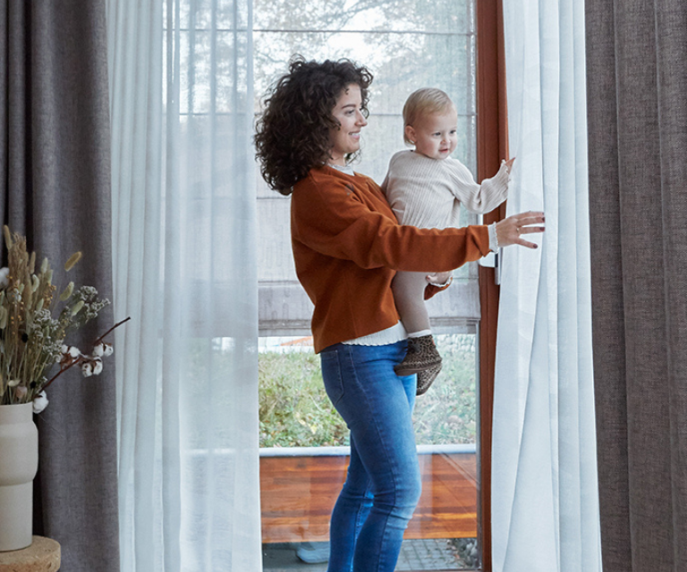 Vrouw met kind in woonkamer met witte vitrages