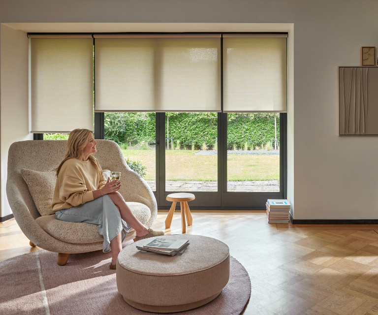 Beige/licht gele rolgordijnen in de woonkamer met een dame op een stoel