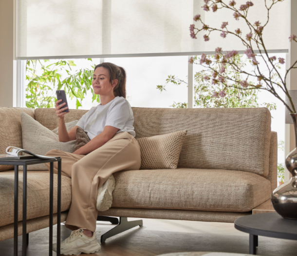 Vrouw op de bank die elektrische witte rolgordijnen bedient