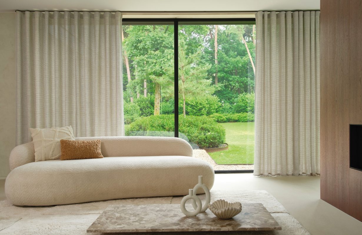 Grijze overgordijnen in de woonkamer met beige bank en licht vloerkleed
