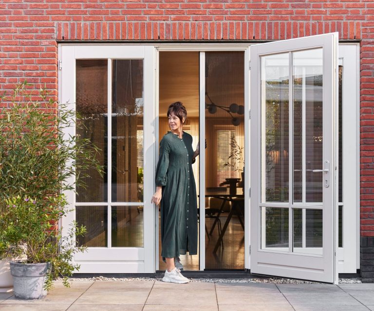 Plisse hordeuren in openslaande deuren met vrouw die naar buiten stapt